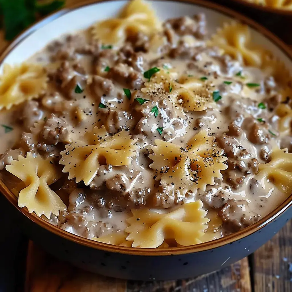Un plat de farfalles nappées d'une sauce au parmesan et viande hachée, garnies de persil et de poivre.