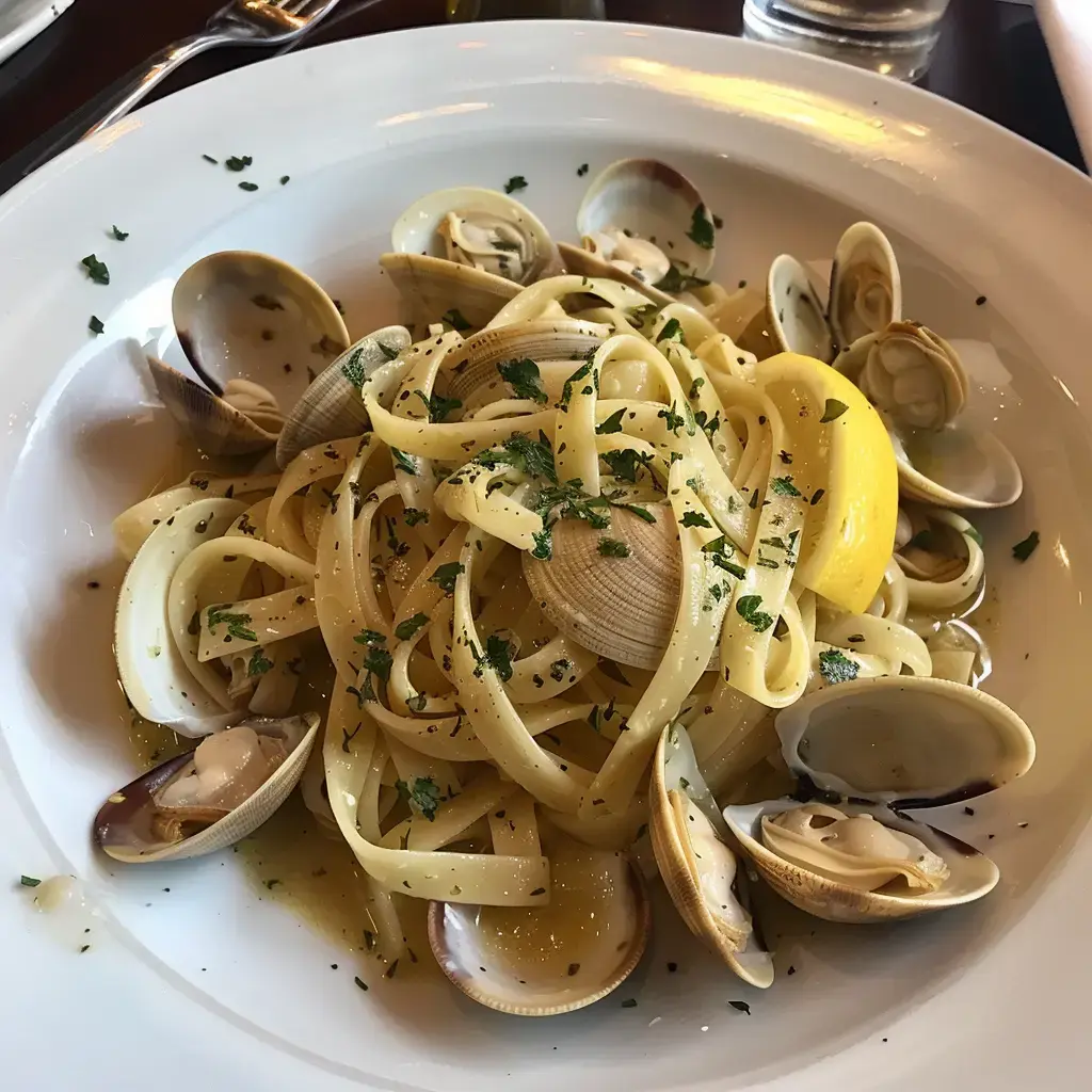 Linguine aux coques servies dans une assiette blanche avec garniture de persil et quartier de citron