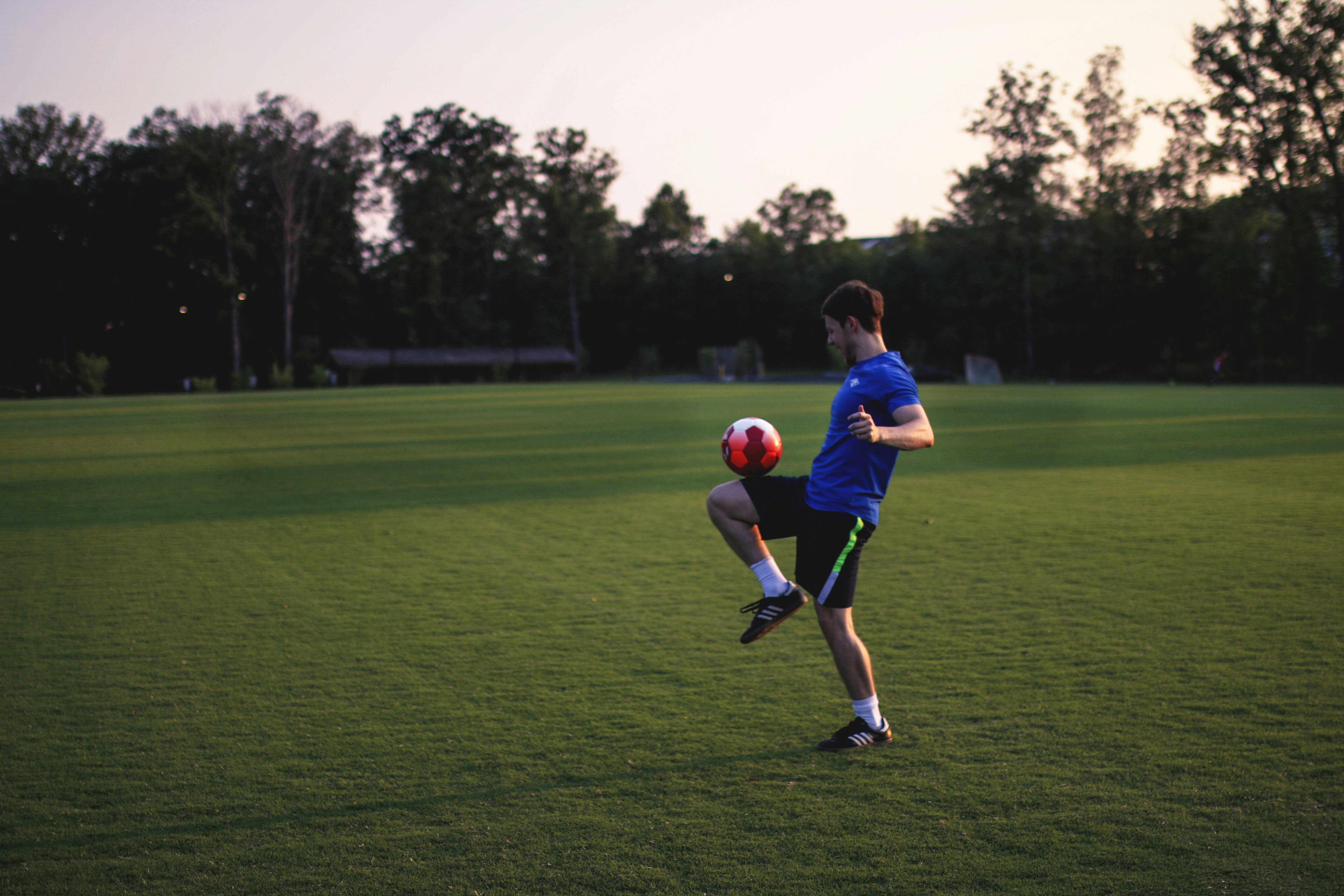 Un jeune homme en train de chuter un ballon de football sur un terrain de football.