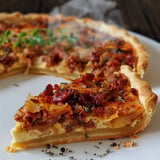 Une tarte appétissante avec des morceaux de viande, des oignons et des herbes, présentée sur une assiette.