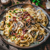 Assiette de tagliatelles crémeuses accompagnées de champignons et de lard croustillant, parsemée de persil et de fromage râpé.