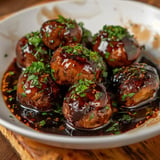 Un bol contenant des champignons rôtis, enrobés de sauce sombre et parsemés de ciboulette fraîche.