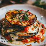 Un gratin d’aubergines dorées superposées avec des tomates et du fromage fondu, décoré de basilic frais.