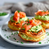 Petits choux garnis de crème au fromage et avocat avec du saumon fumé, joliment dressés avec de la ciboulette, sur un plat blanc chic.