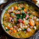 Un bol généreux de soupe aux légumes garnie de tranches de jambon, herbes fraîches et carottes fondantes.