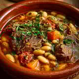 Loubia est un plat traditionnel marocain composé de viande de boeuf, de légumes et de haricots. Dans cette image, on peut voir une portion de Loubia dans un bol en terre cuite, accompagnée de légumes tels que des carottes et des tomates.