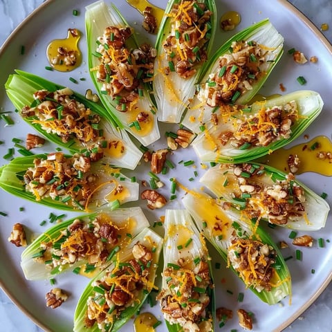 Des feuilles d'endives riches en noix, zestes d'orange et chèvre, subtilement décorées de miel, servis sur un plat blanc.