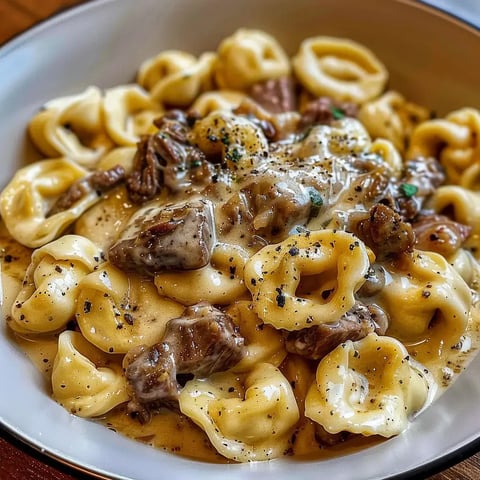 Bol de tortellinis crémeux avec viande et légumes épicés, joliment présenté.