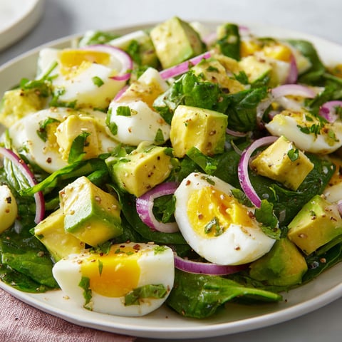 Une assiette garnie de salade d'œufs, avocat et épinards posée sur un plateau.