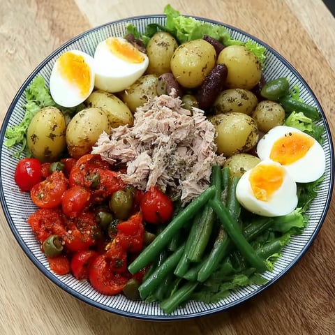 Une salade niçoise revisitée est servie sur un plateau en bois.