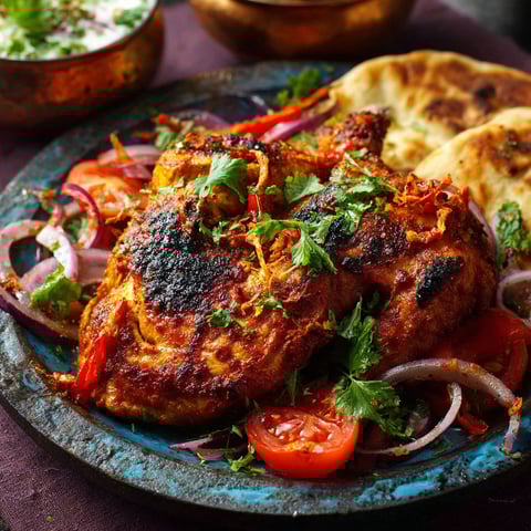 Un poulet grillé avec des légumes verts et des légumes rouges, sert sur un plateau en céramique.